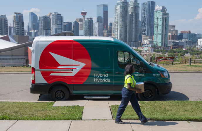 A new Canada Post truck drives on a residential street. The truck is forest green and white and features the red and white Canada Post rondelle logo.
