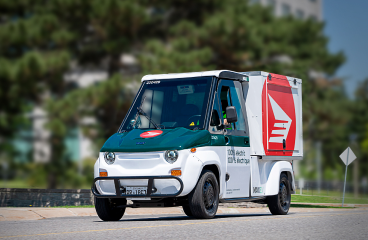 New Canada Post energy efficient delivery vehicles idle in a wet parking lot at sunset.