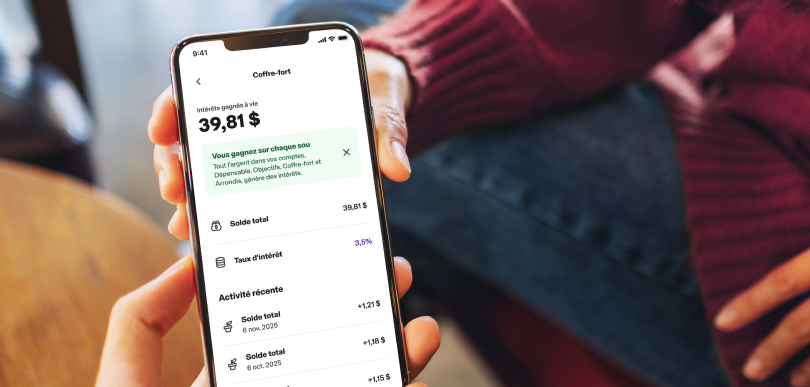 Une personne tient un téléphone intelligent affichant la page « Coffre-fort » du compte MonArgent Postes Canada offert avec Koho.