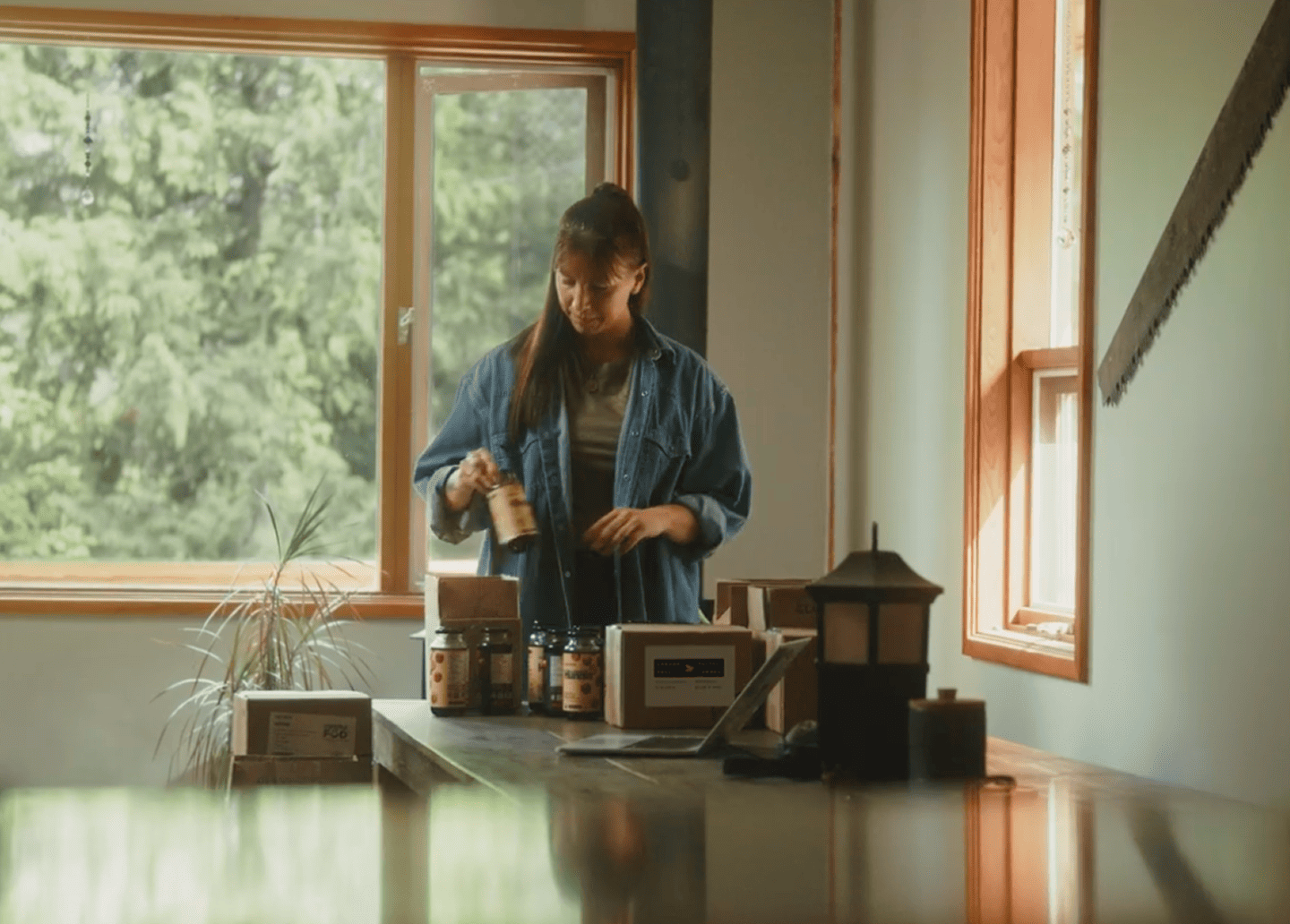 Venessa Stonehouse, cofondatrice et chef de la direction de Mindful Food, place des pots &eacute;tiquet&eacute;s dans des bo&icirc;tes d&rsquo;exp&eacute;dition sur une table, &agrave; c&ocirc;t&eacute; d&rsquo;un ordinateur portable, dans un espace de travail baign&eacute; de lumi&egrave;re naturelle.