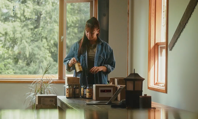 Venessa Stonehouse, cofondatrice et chef de la direction de Mindful Food, place des pots &eacute;tiquet&eacute;s dans des bo&icirc;tes d&rsquo;exp&eacute;dition sur une table, &agrave; c&ocirc;t&eacute; d&rsquo;un ordinateur portable, dans un espace de travail baign&eacute; de lumi&egrave;re naturelle.