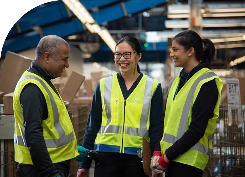 Trois employés de Postes Canada sourient. Ils portent des gilets de haute visibilité.