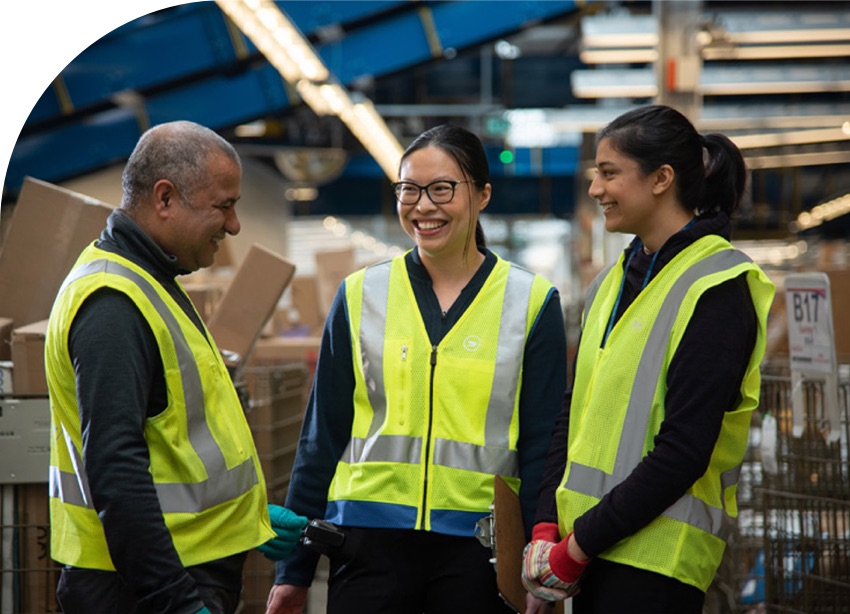 Three Canada Post employees smile. They wear bright yellow safety vests.