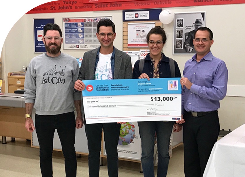 Quatre membres du personnel d’Art City acceptent un chèque de 13 000 $ de la Fondation communautaire de Postes Canada.
