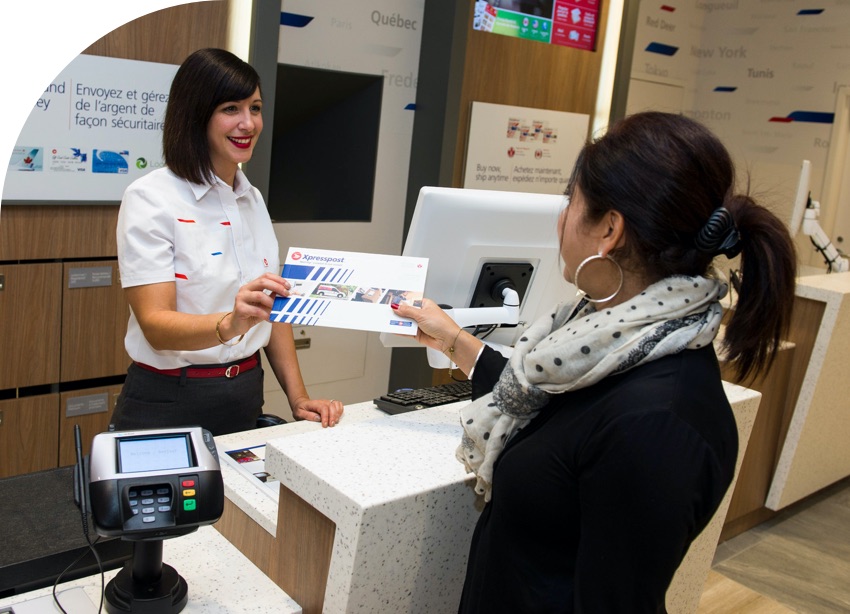 A customer hands a Canada Post team member an Xpresspost envelope at a Canada Post kiosk.