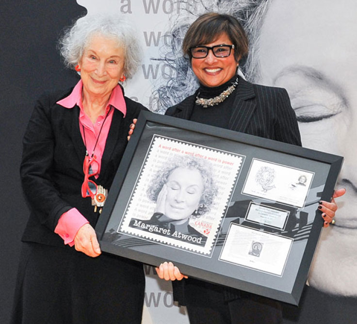 Margaret Atwood et Suromitra Sanatani, présidente du Conseil d’administration de Postes Canada, tiennent un cadre commémoratif mettant en vedette un timbre de Postes Canada de 2021 rendant hommage à Mme Atwood