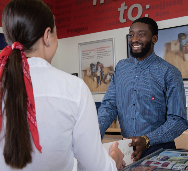 A smiling Canada Post clerk gives a woman her package.