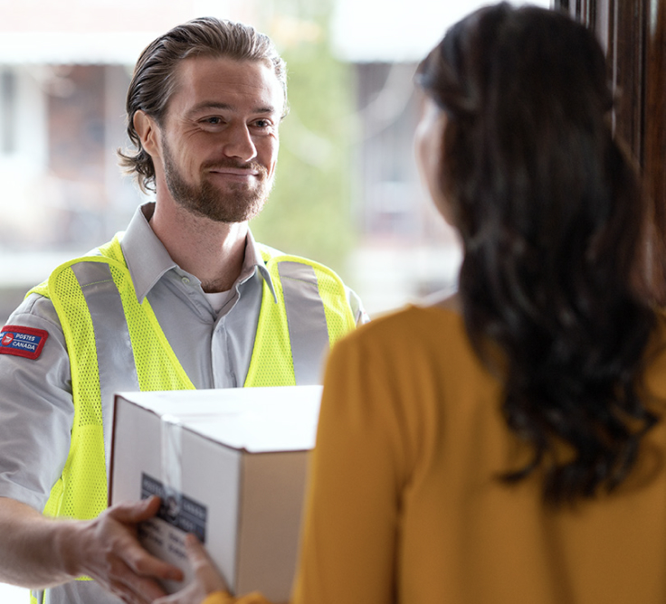 A smiling Canada Post delivery agent gives a woman her package.