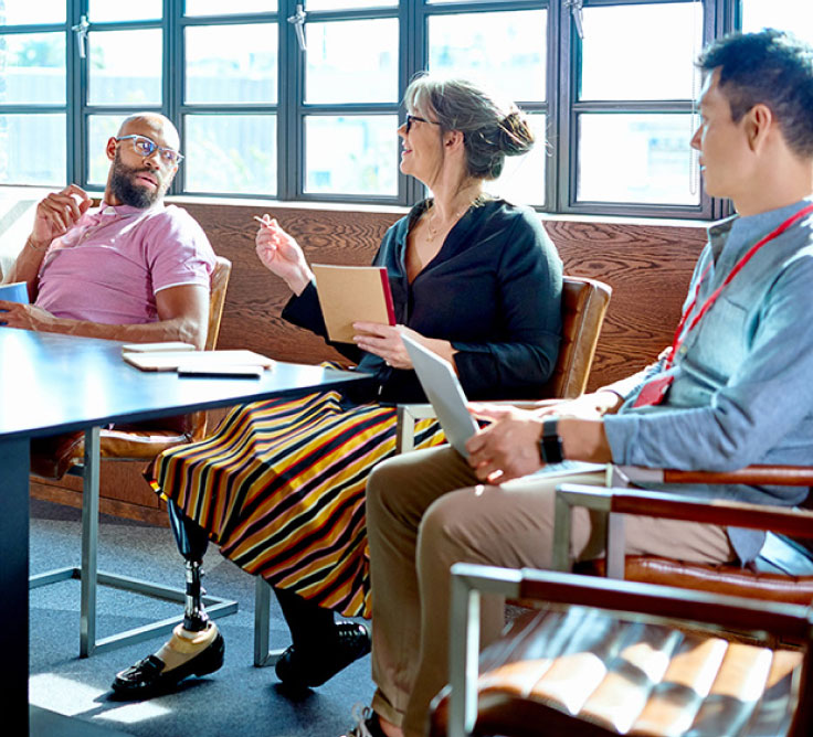 A diverse group of people having a meeting. One person wears a prosthetic leg.