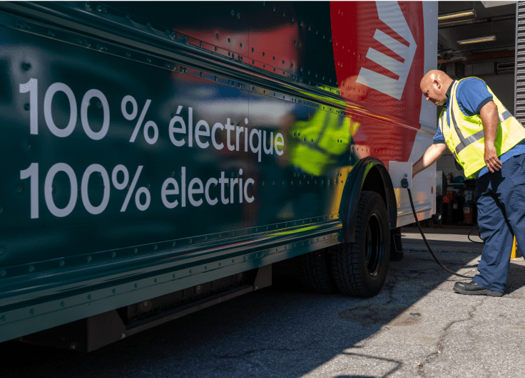 Un employé de Postes Canada vêtu d’un gilet de haute visibilité jaune branche un camion de livraison électrique de Postes Canada