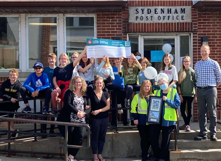Children and staff from Loughborough Public School gather for a photo outside the Sydenham post office holding an oversized cheque from Canada Post Community Foundation.