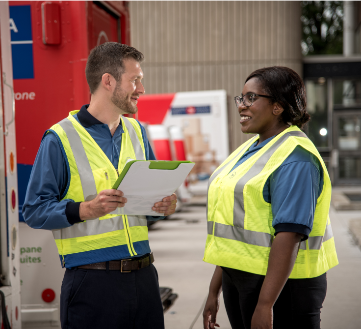 Un employé et une employée de Postes Canada vêtus d’un gilet de haute visibilité jaune discutent dans une installation de Postes Canada