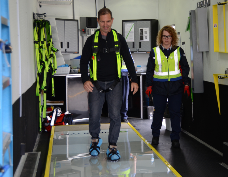 An employee practices walking on a slippery surface, a slip simulator, in a Canada Post facility while a colleague watches him.