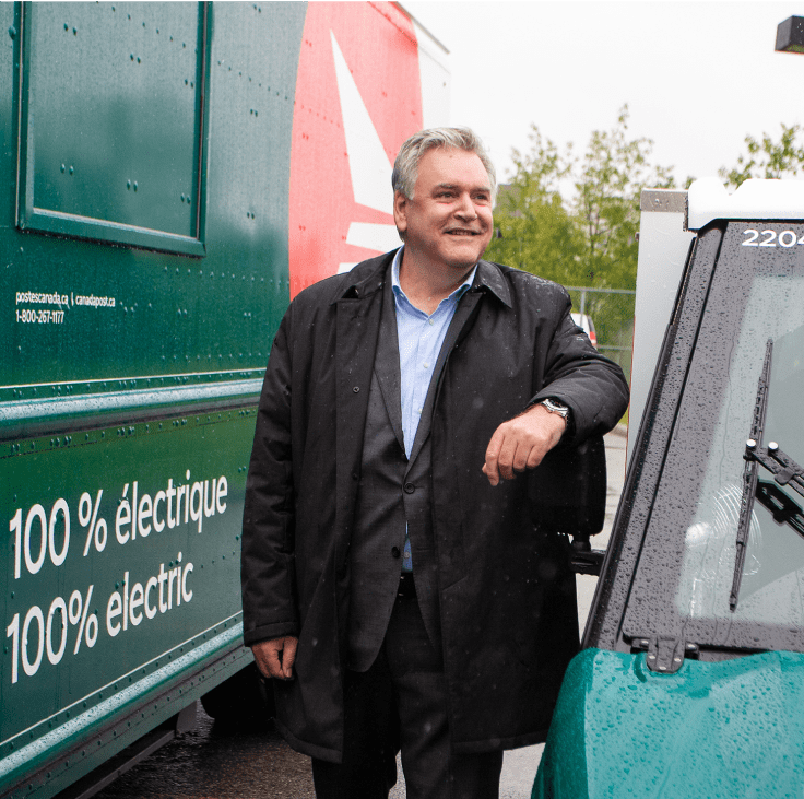 Doug Ettinger, président-directeur général de Postes Canada, se tient entre deux véhicules écologiques.