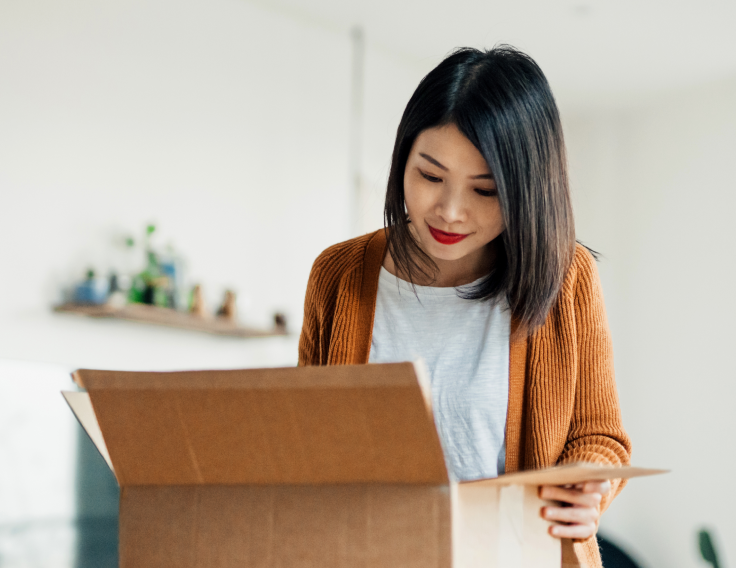 Une femme tient une boîte d’expédition ouverte et regarde à l’intérieur