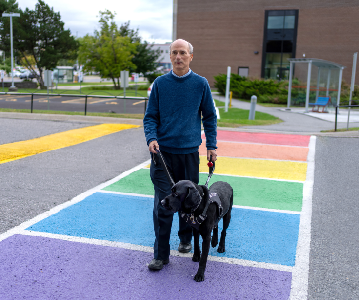 A man crosses a rainbow crosswalk with a guide dog.