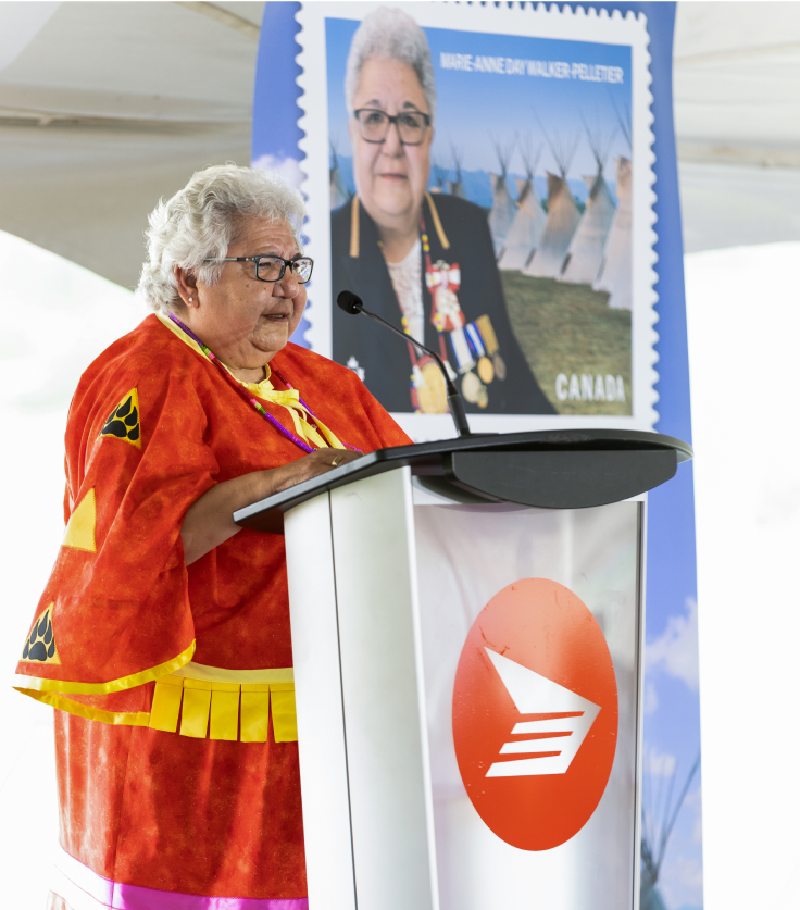 Chief Marie-Anne Day Walker-Pelletier speaks at a podium for the unveiling of her commemorative stamp in Fort Qu'Appelle, Saskatchewan. An enlargement of the stamp is behind her.