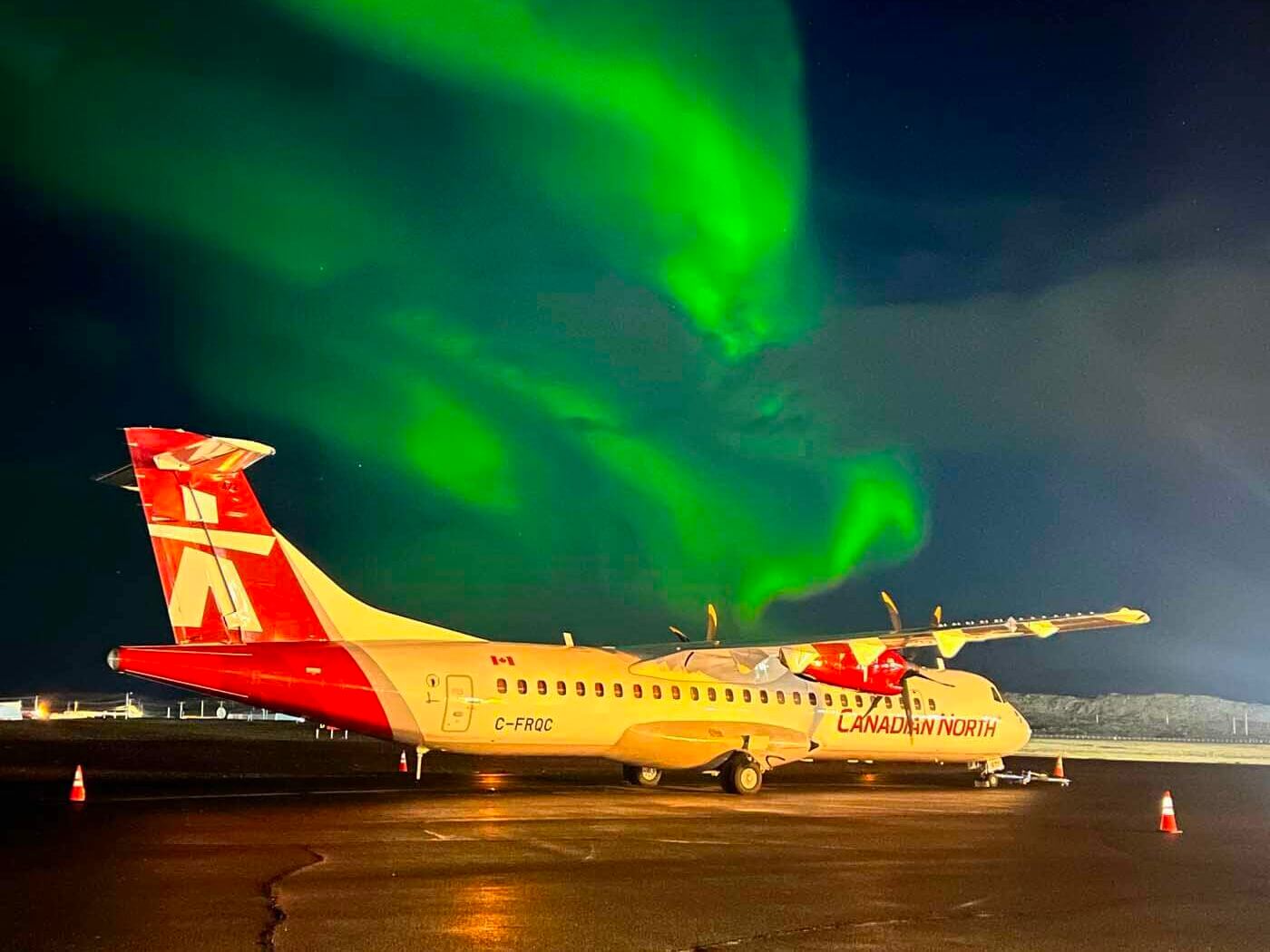 A plane sits on a tarmac in the glow of the Northern Lights.