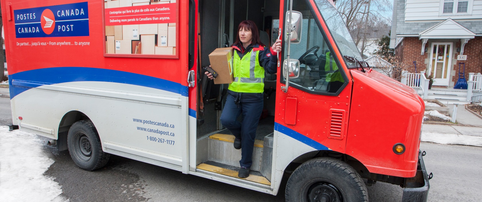 Delivery agent stepping out of a Canada Post truck in a residential neighbourhood to deliver a package