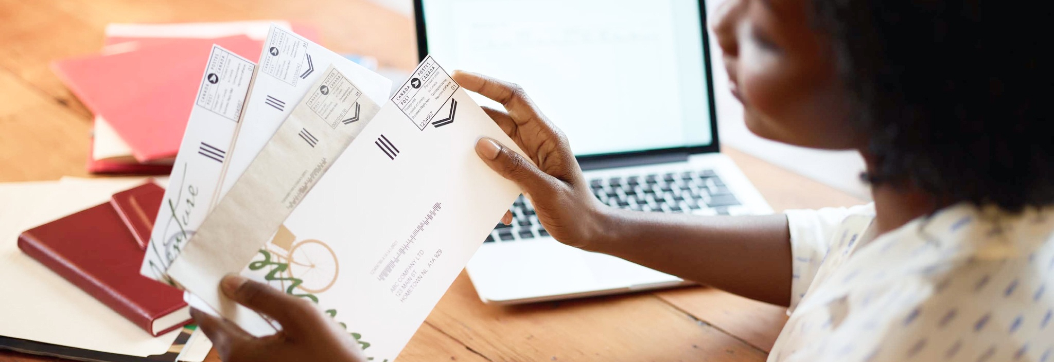 A woman at her desk holds a small stack of business mail. A Canada Post postal indicia is printed on the upper right-hand corner of each envelope.