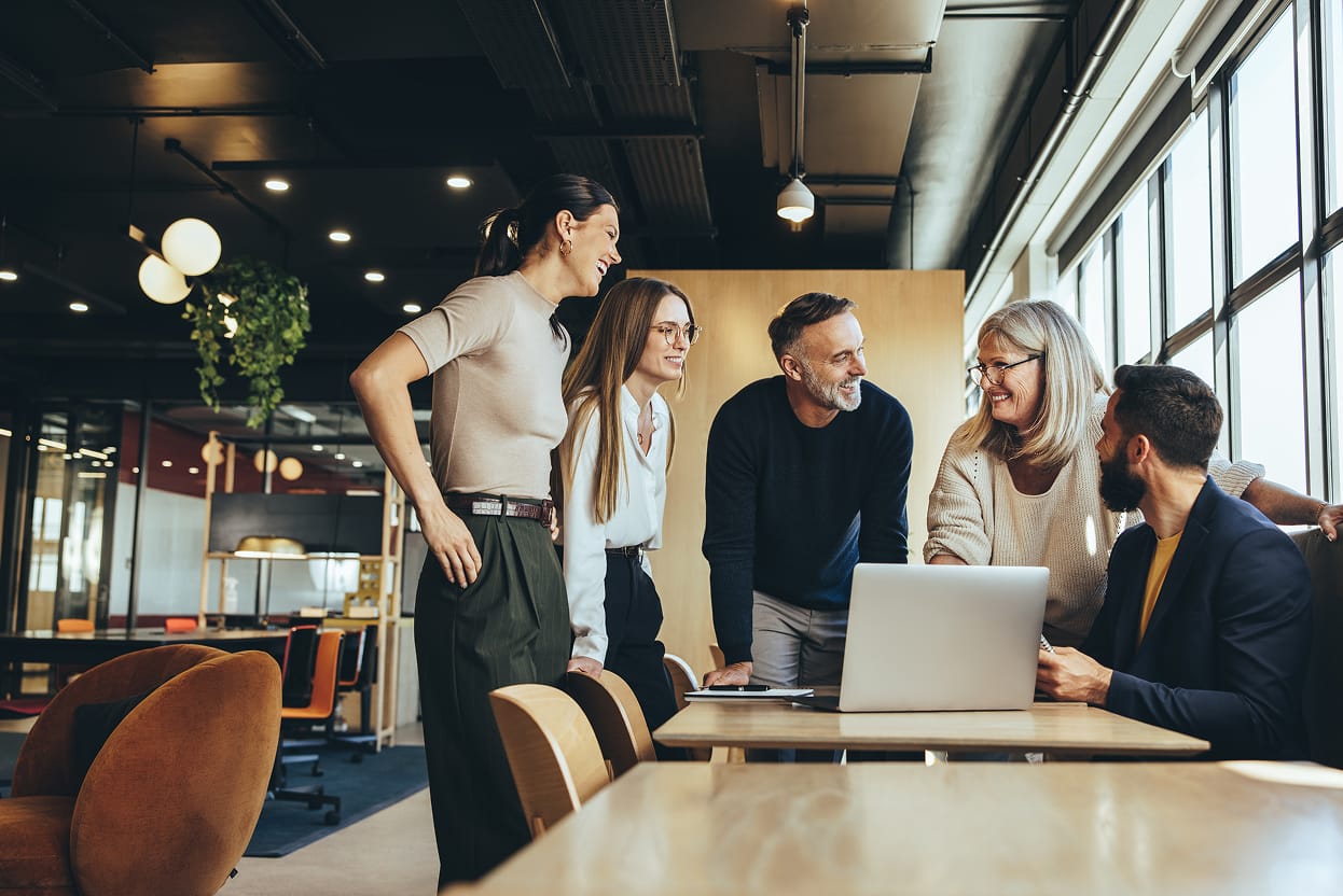 A group of 5 people working collaboratively at a desk.