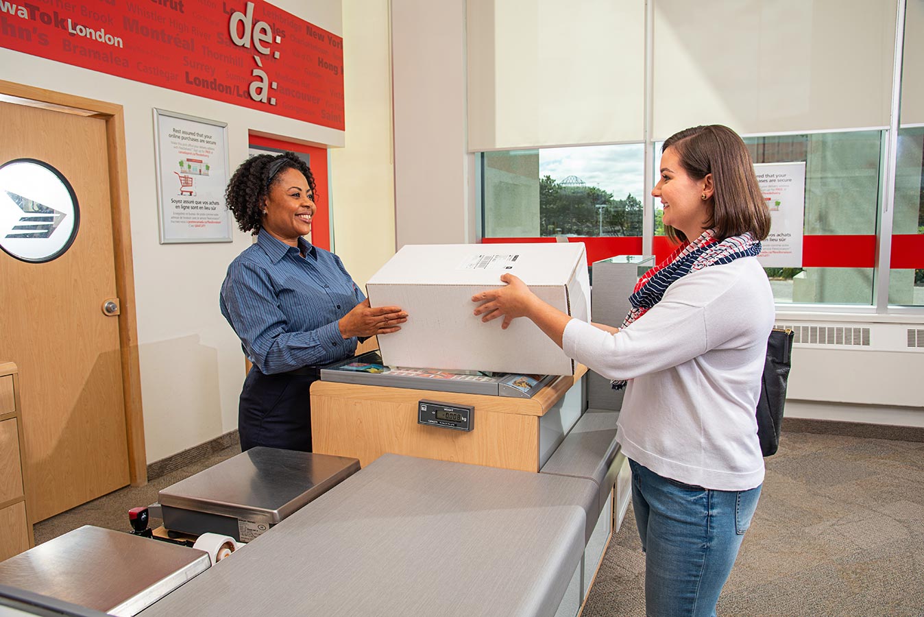 Woman handing a package to a Canada Post retail employee at a post office