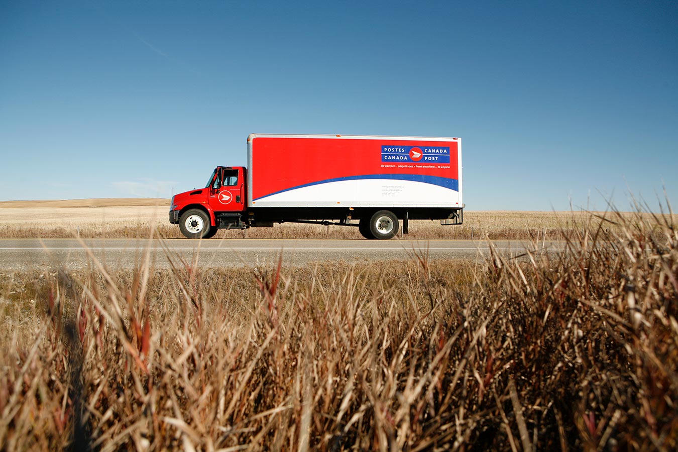 Canada Post delivery truck driving through the prairies under a clear and bright sky