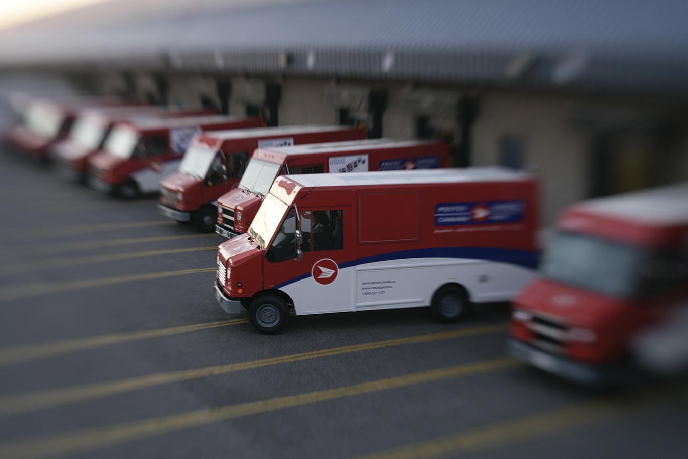 Line of parked Canada Post delivery trucks with one truck pulling out