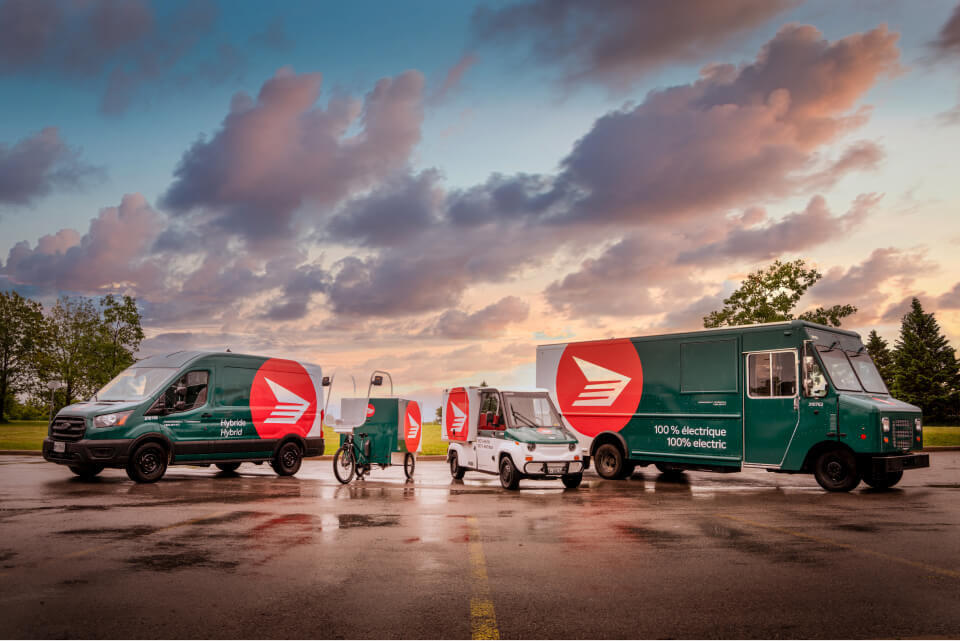 Divers véhicules de livraison hybrides et électriques de Postes Canada sont stationnés en rangée.
