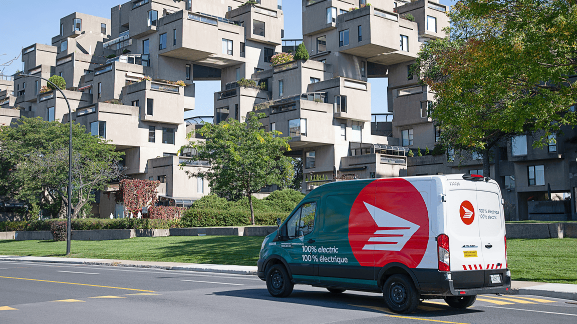 A Canada Post green fleet vehicle drives along an urban road near a modern looking condo development. A Canada Post green fleet vehicle drives along an urban road near a modern looking condo development.