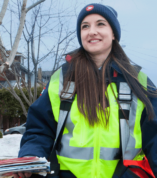 Employée de Postes Canada marchant sur le trottoir en transportant des sacs de courrier.