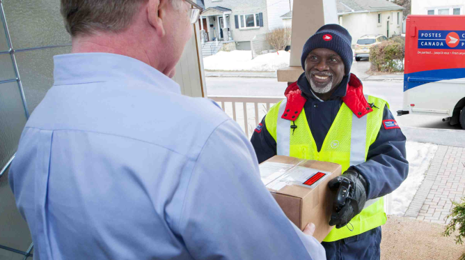 A man receives a package from a Canada Post employee on his doorstep.
