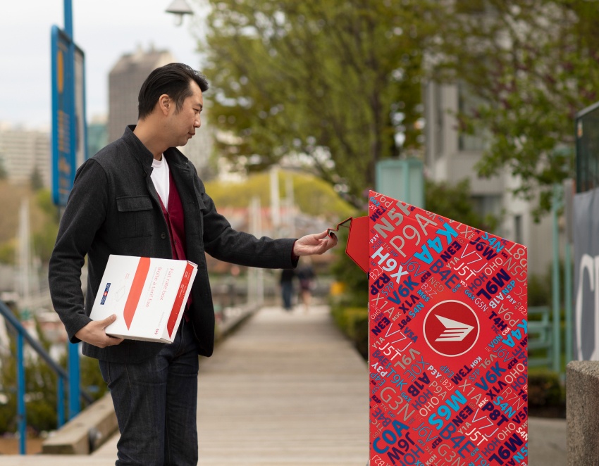 A man deposits a Canada Post flat rate box into a red Canada Post mailbox.