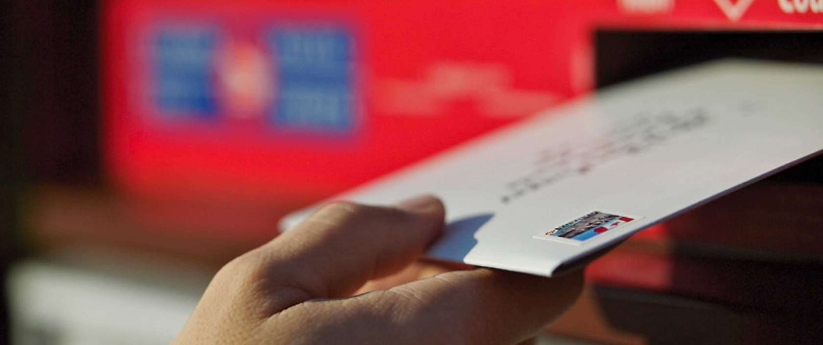 A stamped and addressed envelope is placed in a Canada Post community mailbox to be mailed.