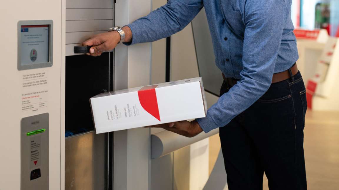 A man uses an automated parcel drop box at a post office to mail a Canada Post flat rate box.