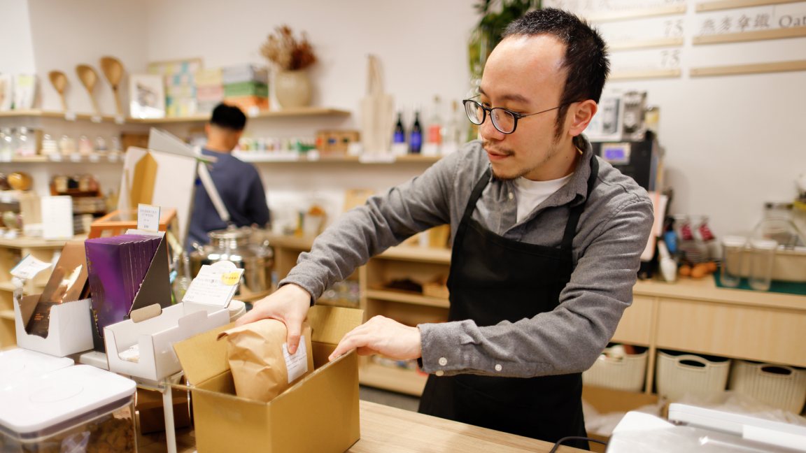 A man accepts a package delivery at the door to his shop.