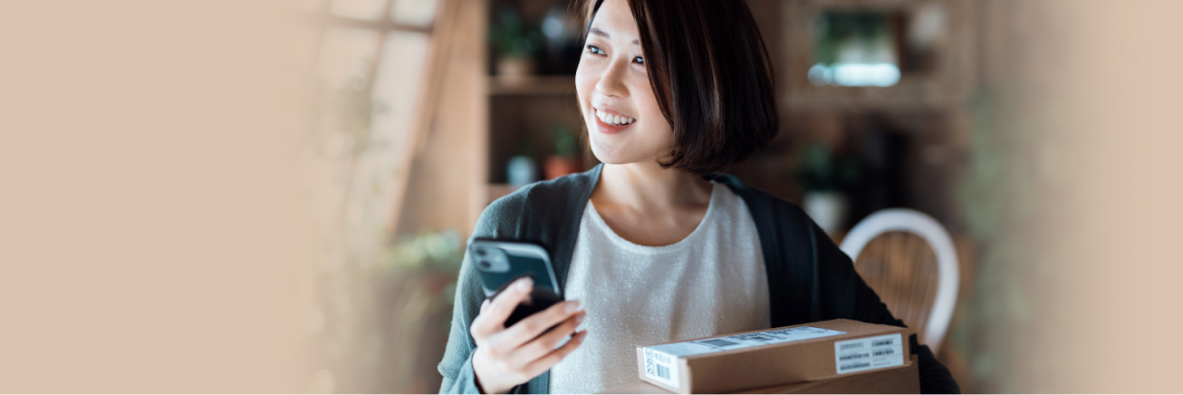 Femme souriante portant des colis tout en tenant un téléphone intelligent d’une main