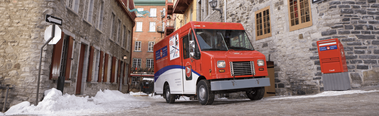 A Canada Post delivery truck parked next to a Canada Post mailbox on a cobblestone street in winter. 