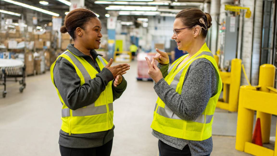 Deux employées d’une installation de tri communiquent en langue des signes, et l’une d’elle porte un appareil auditif. Deux employées d’une installation de tri communiquent en langue des signes, et l’une d’elle porte un appareil auditif.