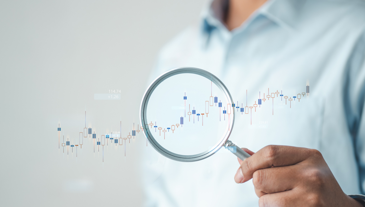 Un homme tient une loupe au-dessus d’un graphique en hausse, soulignant ainsi l’importance de l’analyse des données sur les résultats commerciaux.