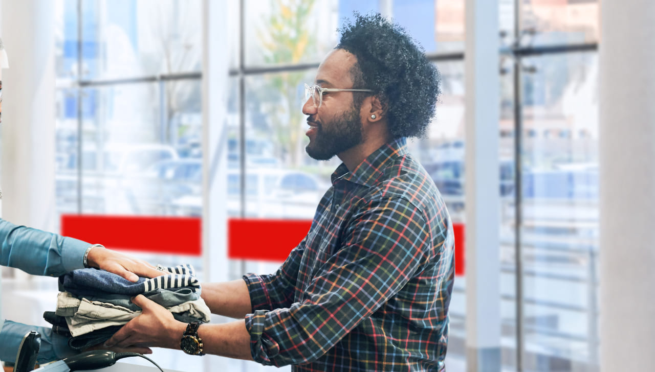 Au comptoir d’un bureau de poste, un homme remet des vêtements pliés pour un retour.