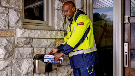 Un facteur de Postes Canada effectue une livraison dans une boîte aux lettres à domicile.