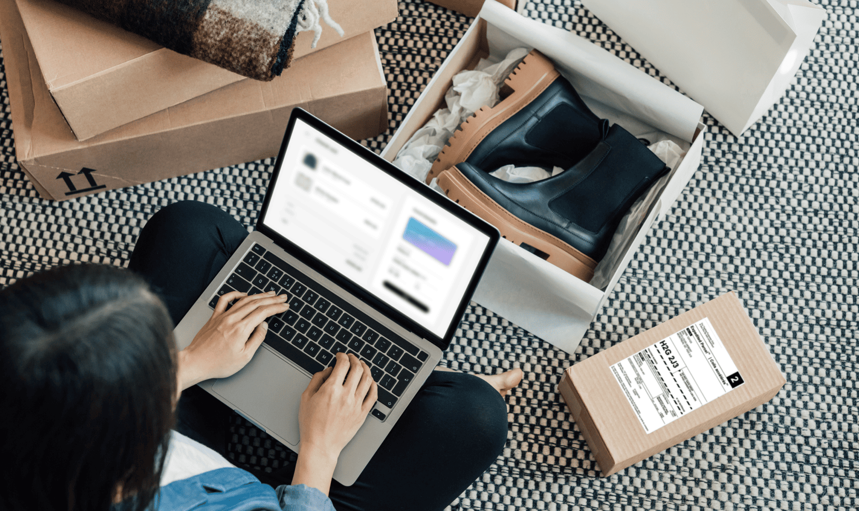 Une femme, assise par terre devant son portable, prépare le retour d’une paire de bottes achetées en ligne.