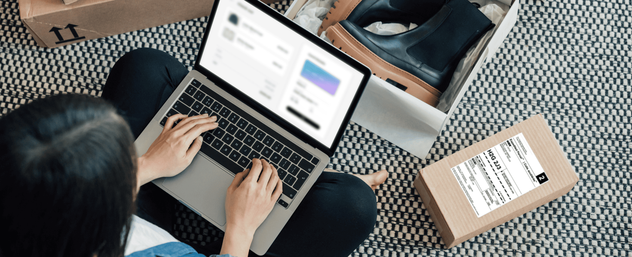 Une femme, assise par terre devant son portable, prépare le retour d’une paire de bottes achetées en ligne.