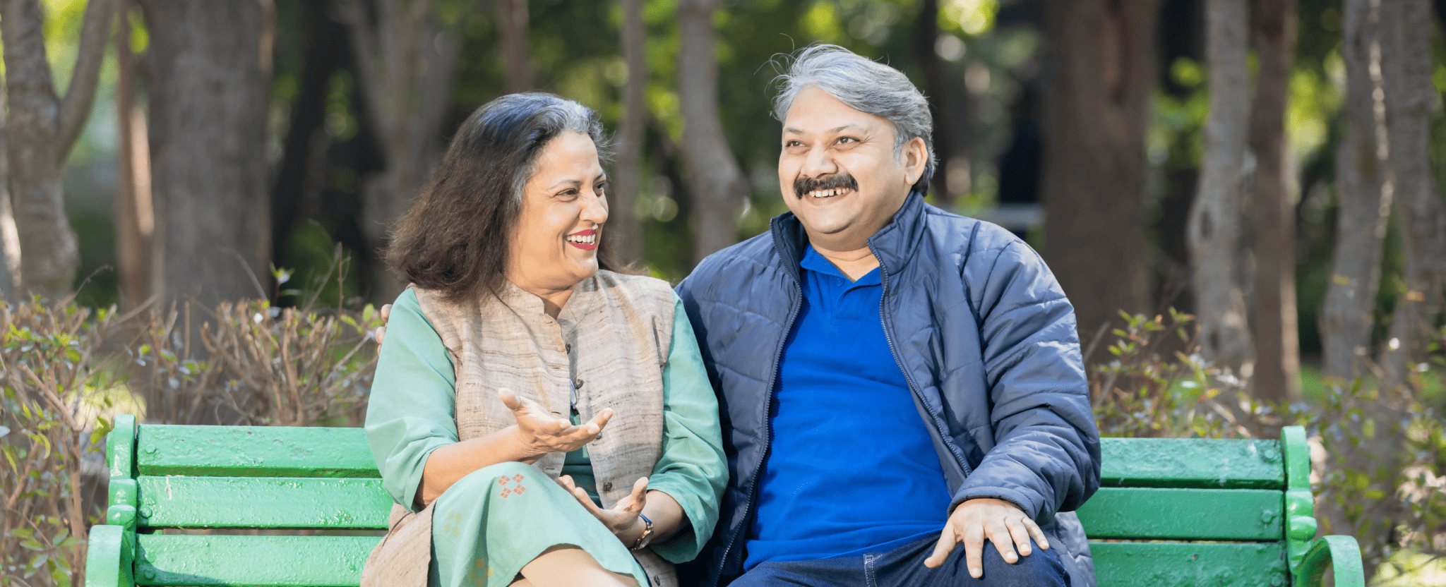 Un couple d’âge mûr souriant est assis sur un banc de parc.