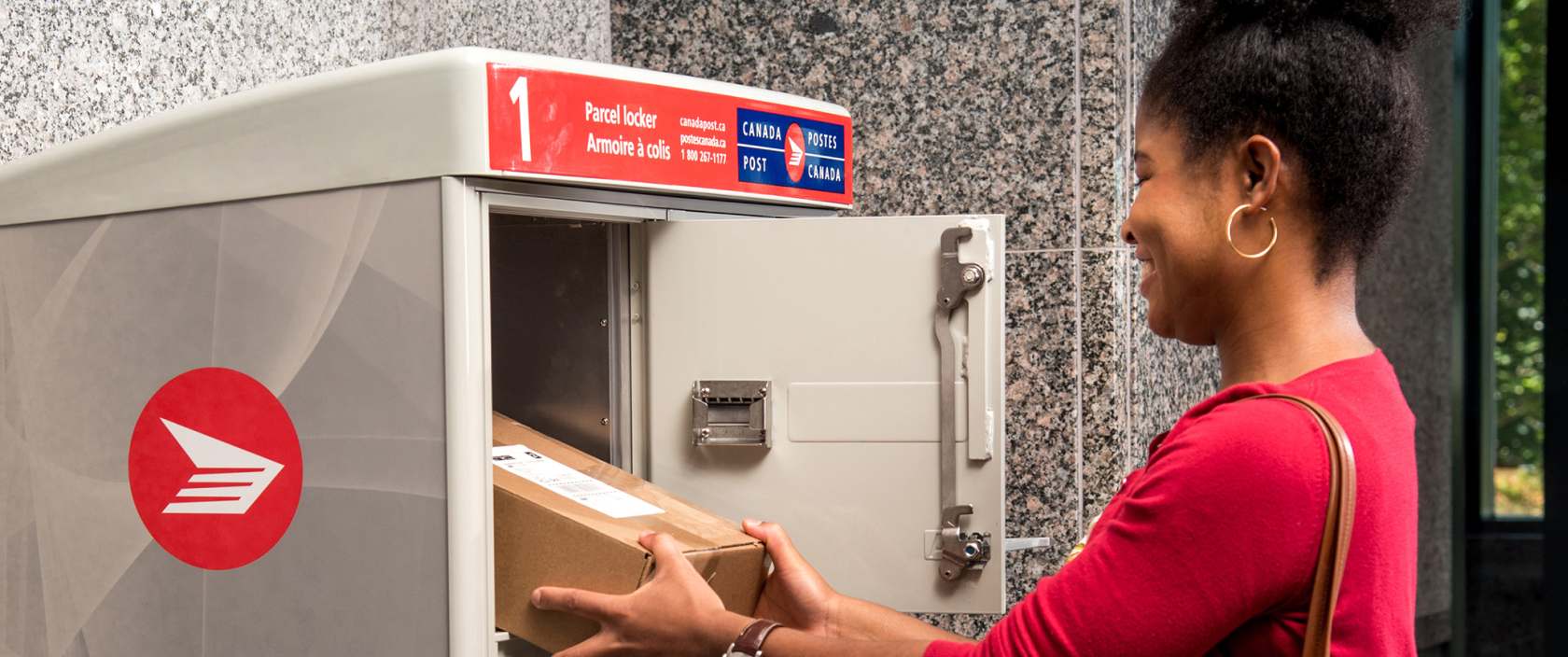 Une femme récupère son colis dans l’armoire à colis de Postes Canada dans la salle de courrier de son immeuble d’habitation