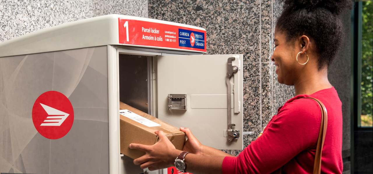 Une femme récupère son colis dans l’armoire à colis de Postes Canada dans la salle de courrier de son immeuble d’habitation
