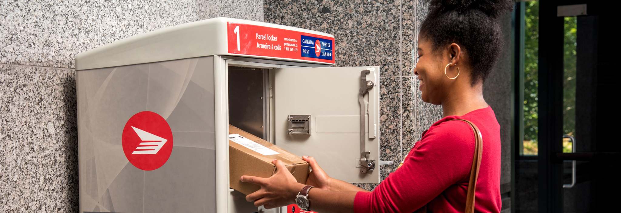 Une femme récupère son colis dans l’armoire à colis de Postes Canada dans la salle de courrier de son immeuble d’habitation