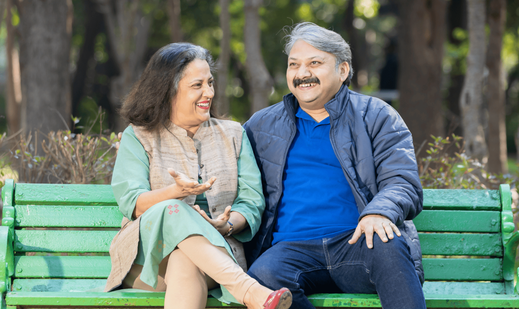 Un couple d’âge mûr souriant est assis sur un banc de parc.
