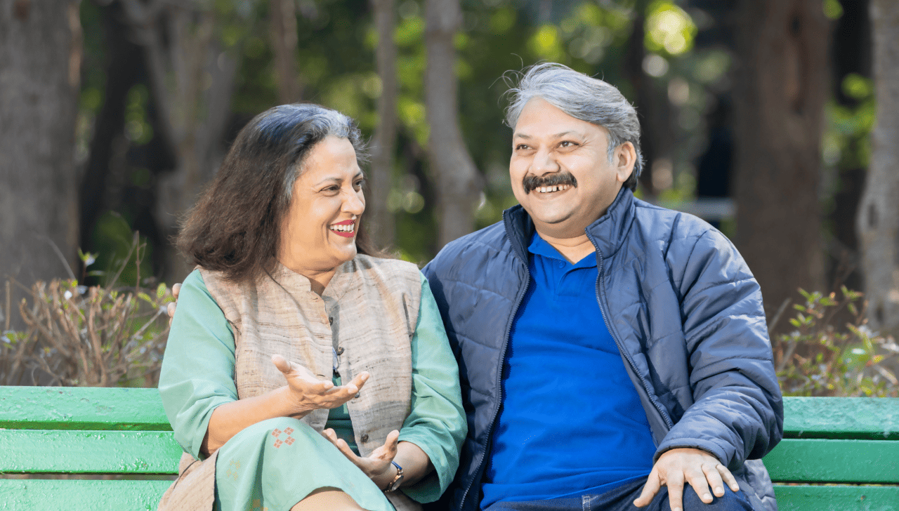 Un couple d’âge mûr souriant est assis sur un banc de parc.